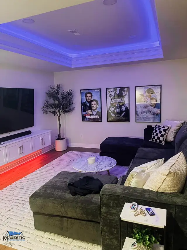 Shelby Township basement lounge with a sectional sofa, wall-mounted TV, framed posters and color-changing cove lighting