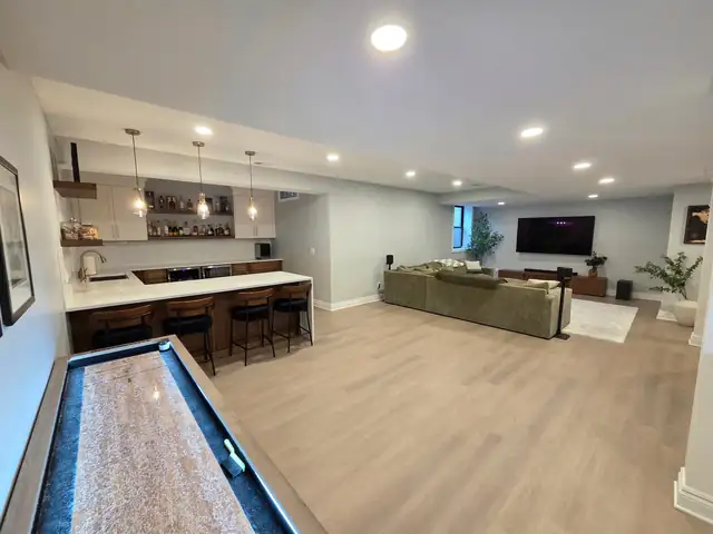 Finished basement in Troy, MI with a shuffleboard table, a bar with seating and an open lounge area