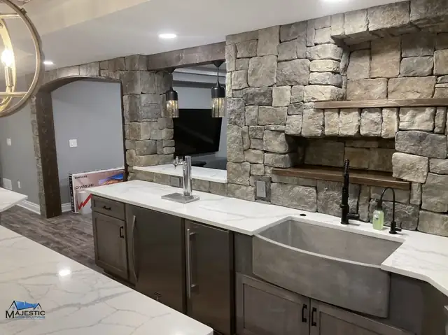 Novi basement kitchenette with a stacked stone wall, farmhouse sink, gray cabinets and white stone countertops