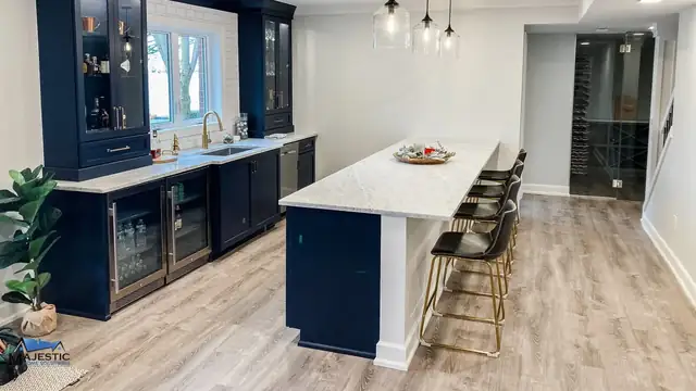 Northville basement with navy blue bar cabinets, glass-front display shelves and a white island with gold bar stools