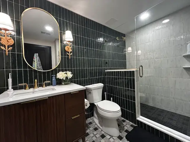 Bathroom with dark green vertical wall tile, a wood vanity, brass-framed mirror and a frameless glass shower