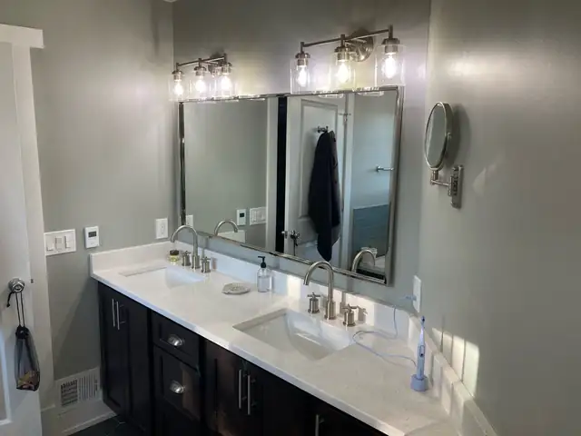 Clinton Township primary bathroom remodel with a dark double vanity, white counter, two framed mirrors and vanity light bars