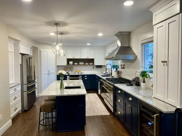 Remodeled kitchen with navy lower cabinets and island, white upper cabinets, glass pendant lights and a stainless range hood